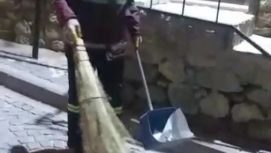 Hem çevreyi temizliyor hem de sokak kedisine süpürgesi ile masaj yapıyor